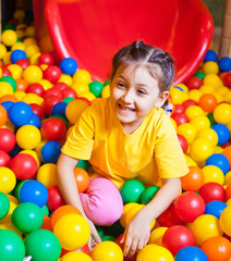 Fototapeta na wymiar Happy little girl playing and having fun at kindergarten with colorful balls in play center