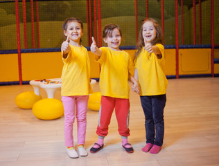 Obraz premium Three funny girls show thumb up in children's entertainment center