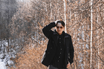 Fototapeta na wymiar Portrait of a young man in a coat and sunglasses walking in the woods. Travel through the mountains and forests. Young man walking in the forest Sunny spring day.
