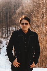Portrait of a young man in a coat and sunglasses walking in the woods. Travel through the mountains and forests. Young man walking in the forest Sunny spring day.