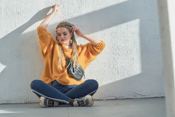 a woman with african pigtails is sitting on the floor. Waist bag on the shoulder, blonde with African braids.