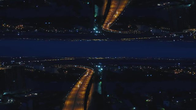 Aerial night view of a river bridge with moving cars and the city with night lights, mirror horizon effect. Media. Stunning landscape of night city and the bridge across the river, inception theme.