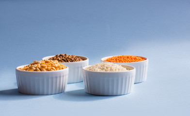 Assorted different cereals on a blue background. Buckwheat, lentils, rice, peas in plates on top, copy of the place. Healthy eating concept
