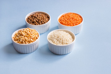 Assorted different cereals on a blue background. Buckwheat, lentils, rice, peas in plates on top, copy of the place. Healthy eating concept