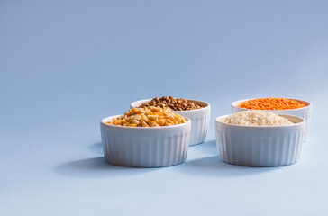 Assorted different cereals on a blue background. Buckwheat, lentils, rice, peas in plates on top, copy of the place. Healthy eating concept