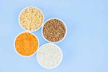Assorted different cereals on a blue background. Buckwheat, lentils, rice, peas in plates top view, copy space