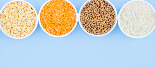 Assorted different cereals on a blue background. Buckwheat, lentils, rice, peas in plates top view, copy space