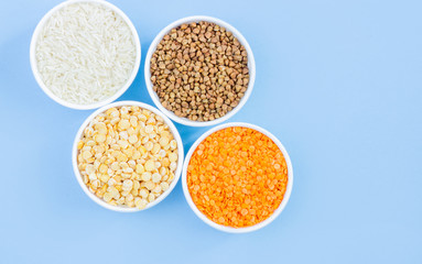 Assorted different cereals on a blue background. Buckwheat, lentils, rice, peas in plates top view, copy space