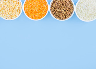 Assorted different cereals on a blue background. Buckwheat, lentils, rice, peas in plates top view, copy space
