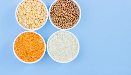 Assorted different cereals on a blue background. Buckwheat, lentils, rice, peas in plates top view, copy space