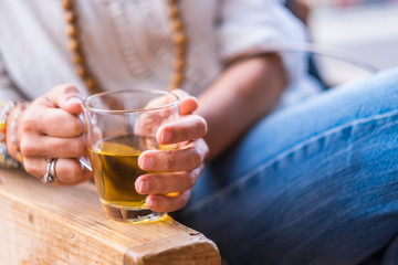 Close up of woman with coloured fashion accessories and jeans taking holding a glass of healthy tea for afternoon break time - beverage and relaxing activity