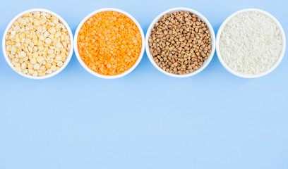 Assorted different cereals on a blue background. Buckwheat, lentils, rice, peas in plates top view, copy space