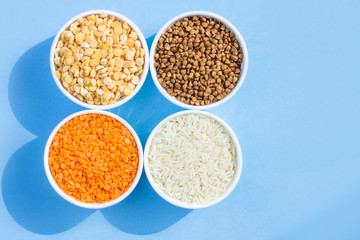 Assorted different cereals on a blue background. Buckwheat, lentils, rice, peas in plates top view, copy space