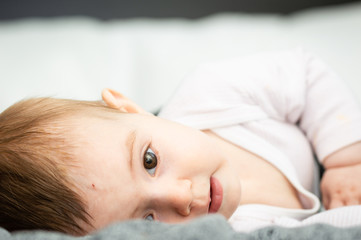 Obraz na płótnie Canvas adorable blond baby lying on back on white bed