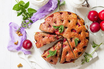 Delicious dessert plum pie, sweet delicious holiday plums cake with nuts on the white kitchen table. Top view flat lay background.