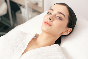 Serious woman in bathrobe lying on the medical couch