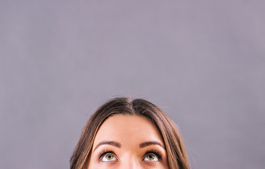 Closeup beautiful young woman looking up on blank copy space isolated on gray background....