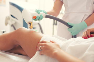 Medical worker using laser tool for removing stretches on the leg of client