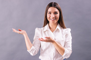 Happy young woman in white shirt presenting blank space with open palms while standing isolated on...