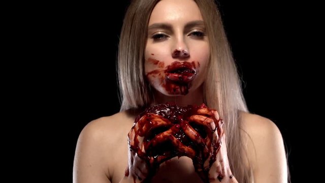 portrait of a girl who chews a piece of meat torn from the heart, which she holds in front of him. The girl's hands and face are stained with blood.