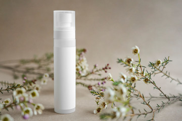White cosmetic bottle on beige background decorated with white flowers