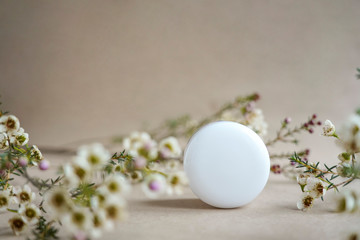 White  round cosmetic jar on a beige background decorated with white flowers