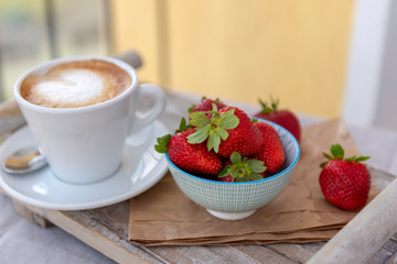 Fresh organic strawberry and cappuccino on a wooden tray. Breakfast outdoors on the balcony.