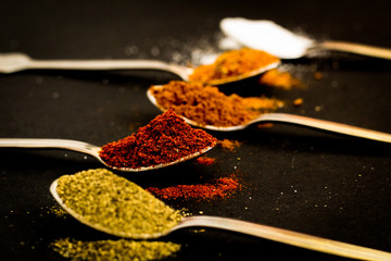 Spice concept: different spices on the spoons, selective focus, black background