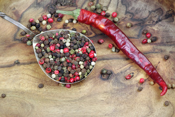 mixture of peppers and red chilli pepper in a spoon on a wooden table. close up.