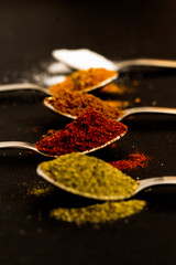 Kitchen concept: Variety of spices, silver spoons, black background, selective focus