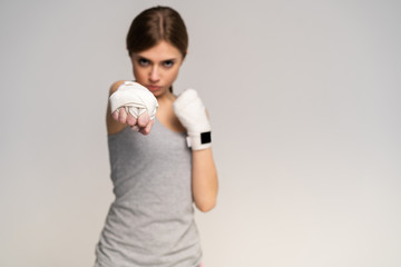 Beautiful boxer girl wearing sportive clothing and gloves practicing in the studio over gray background, athletic body, healthy lifestyle.