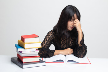 Exhausted Asian woman got headache read a book with books on table.