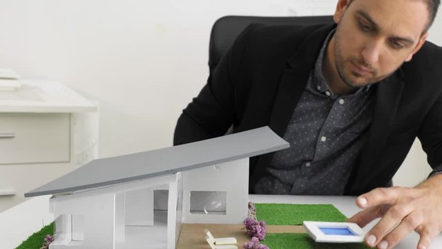 Dolly shot of Businessman fixes the architecture of a house model with swimming pool