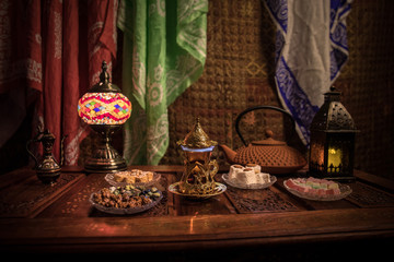 Arabian tea in glass with eastern snacks on vintage wooden surface. Eastern tea concept. Low light lounge interior with carpet. Empty space.