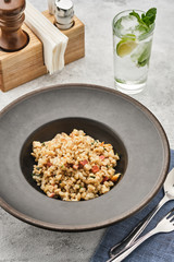 Barley porridge with chicken and bacon in a dark plate on a light table