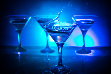 Martini cocktail glass in hand splashing on dark toned smoky background or colorful cocktail in glass with splashes and olives. Party club entertainment. Mixed light. Selective focus