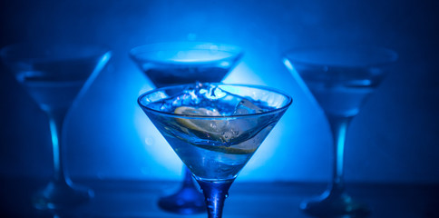 Martini cocktail glass in hand splashing on dark toned smoky background or colorful cocktail in glass with splashes and olives. Party club entertainment. Mixed light. Selective focus