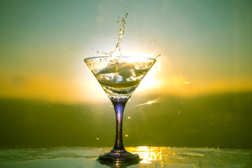Martini cocktail glass in hand splashing on dark toned smoky background or colorful cocktail in glass with splashes and olives. Party club entertainment. Mixed light. Selective focus