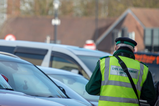 civil enforcement officer or traffic warden writes out parking ticket for vehicle in UK