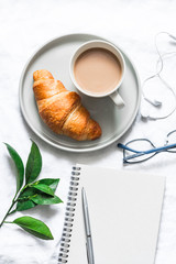 Morning plan. Coffee, croissant and a clean empty notebook on a light background, top view. Flat lay, copy space