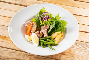 tuna salad with egg, tomatoes, red onions and green beans, wooden background