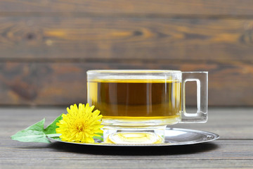 Dandelion tea in transparent cup on wooden background