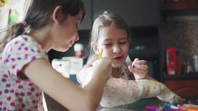 children paint a broken arm in a bandage. sister tries to cheer up and hang out a sick sister.