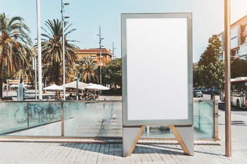 A blank mockup of an urban advertising poster near the metro entrance; white billboard placeholder template on the city street; an empty banner mock-up near the road and underground passage