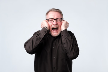 Senior man in red shirt plugging ears with fingers