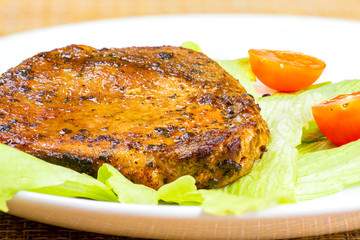 Steak meat with tomato and lettuce salad leaf and fork in a white plate