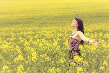 Naklejka na ściany i meble Happy beautiful woman in free summer love of youth wellbeing. Attractive young beauty girl enjoying the warm sunny sun in nature rapeseed field takes time feeling sustainability and contemplation