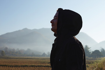 Profile close up portrait of Caucasian male traveller dressed in black jacket with hood, looking at distance, admiring nice scenery, breathing fresh morning air in mountains, enjoying nature alone.