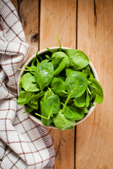 Baby spinach in a bowl on wooden table, top view