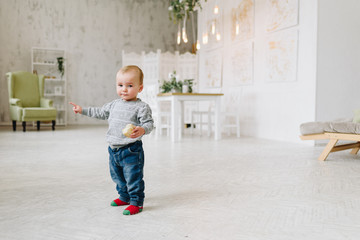 Adorable caucasian toddler boy standing holding a snack. Kid is wearing jeans and a sweater. First steps.